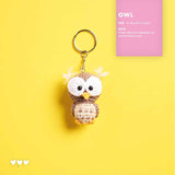 A crochet owl keychain with a gold split ring, displayed on a bright yellow background next to a pink patterned card containing knitting instructions and patterns.