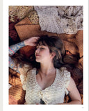 A photo showing a woman lying on a bed of crocheted garments, wearing a cream crochet top.