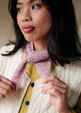 Woman wearing a knitted pink scarf with pattern book open to a scarf-making tutorial.