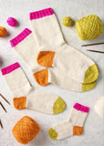 A printed knitting pattern spread sheet for 'Top-Down Doodle Socks' showing the recipe text on the left and several knitted socks with yarn balls on a light surface on the right.