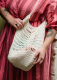 Person holding a crocheted market bag and bottle holder with text on the left side.