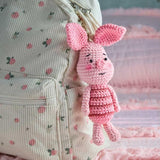 Acrocheted pink piglet doll with a floral backpack in the background.