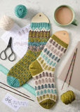 Photo features two hand-knit socks with multicolor patterns, yarn balls, knitting needles, a mug of coffee, and paper on a light surface.