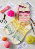 Knitted socks with colorful patterns next to knitting patterns and tools on a light surface.