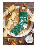 Knitted green and white stocking with wooden holder on a wooden table, surrounded by gift-wrapped items.