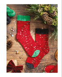 Knitted Christmas socks on a wooden surface with festive decorations and a pattern guide.