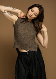 Woman in a textured top and black pants against a brown background.