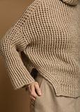 Beige crocheted sweater worn by a person on a brown background.