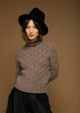 Woman wearing a brown sweater and black hat against a brown background.