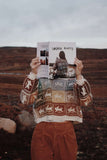 Person holding a book in front of their face with a scenic background