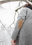 Person wearing a gray jacket with a textured elbow patch in a snowy landscape.