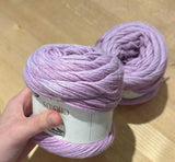 Two skeins of purple yarn on a wooden surface with a hand holding one skein.