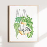 Framed artwork of a cat in a hammock with plants on a white wall