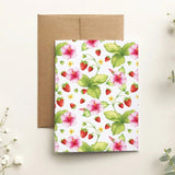 Floral and strawberry patterned card with a brown envelope on a light background with white flowers.